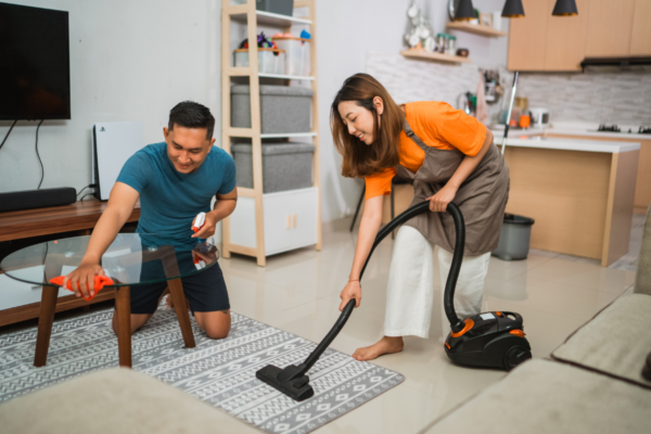 couple cleaning. the wife is hoovering and the husband is polishing a glass table